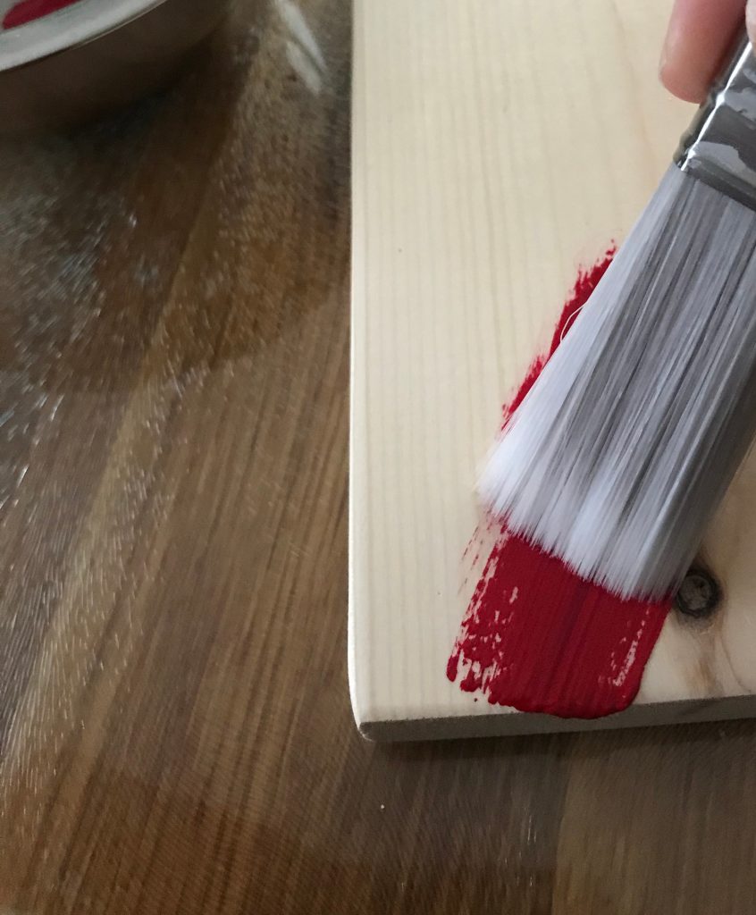 Paint brush adding red paint to sanded piece of wood